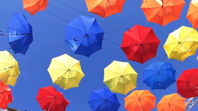 Low angle view on colorful umbrellas hanging in the air against blue sky. Concept of holiday, urban beauty, joy and arts.