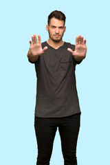 Man with black shirt making stop gesture and disappointed over blue background