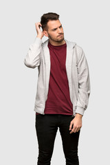 Man with sweatshirt having doubts while scratching head over grey background