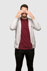 Man with sweatshirt covering eyes by hands. Surprised to see what is ahead over grey background