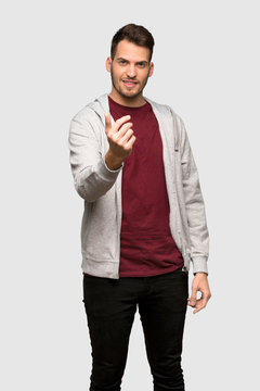 Man with sweatshirt inviting to come with hand. Happy that you came over grey background