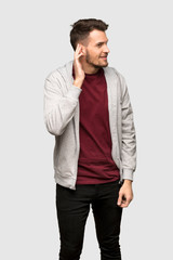 Man with sweatshirt listening to something by putting hand on the ear over grey background