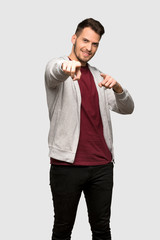 Man with sweatshirt points finger at you while smiling over grey background