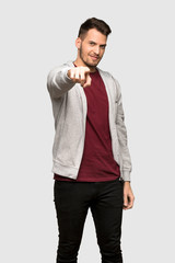 Man with sweatshirt points finger at you with a confident expression over grey background