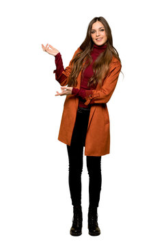 Full-length shot of Young woman with coat extending hands to the side for inviting to come on isolated white background
