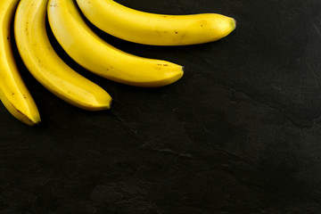 Tabletop view - four bananas on black stone like board, space for text in down right corner.