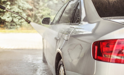 Side of silver car washed in self serve carwash, high pressure jet water spraying to metal, sun lit...
