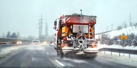 Orange highway maintenance gritter truck spreading de icing salt on road. Dangerous driving...