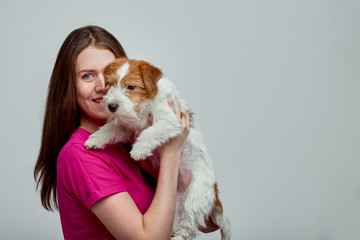 Beautiful girl with a jack russell terrier on her hands on a gray background, copy space