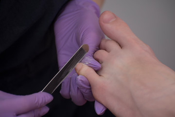 Processing toenails. Gloved hands with a nail file for manicure. Close-up
