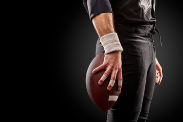 Mid section of American football player with ball against black, copy space, side view - Powered by Adobe