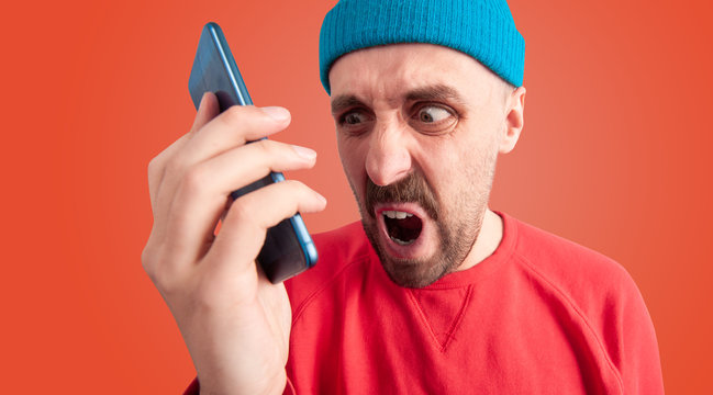Annoyed man with distorted face shouting at his cellphone