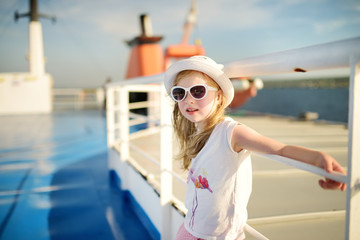 Adorable young girl enjoying ferry ride staring at the sea on sunset. Child having fun on summer...