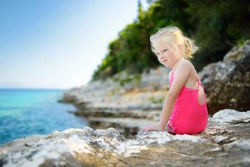 Fototapeta na wymiar Cute little girl having fun at Emplisi Beach, picturesque stony beach in a secluded bay, with clear waters popular for snorkelling.