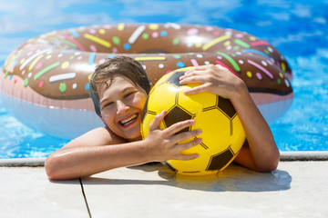 Happy cute little boy teenager in swimming pool. Active games on water, vacation, holidays concept. Chocolate donut. Cool fun summer holidays for children.