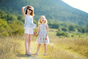 Fototapeta premium Two cute young sisters laughing and hugging on warm and sunny summer day during family vacations in Greece