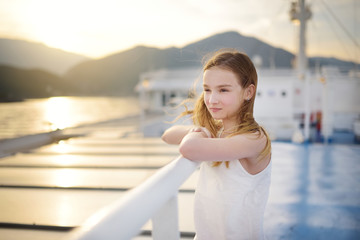 Adorable young girl enjoying ferry ride staring at the sea on sunset. Child having fun on summer family vacation in Greece.