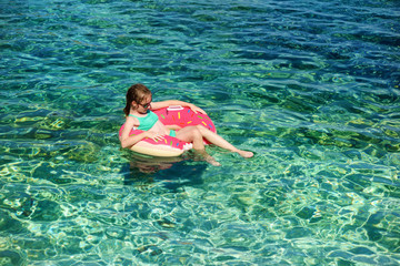 Aerial top down view of cute young girl floating on toy ring at Emplisi Beach, picturesque stony beach in a secluded bay, with clear waters popular for snorkelling.