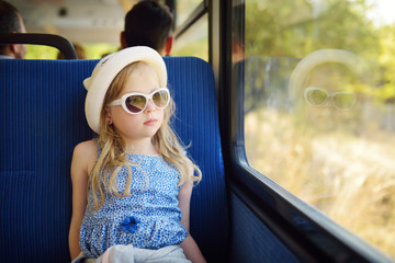 Cute young girl traveling by train on summer day. Child sitting by the window of railway wagon and looking outside.