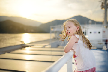 Adorable young girl enjoying ferry ride staring at the sea on sunset. Child having fun on summer family vacation in Greece.