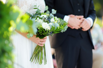 Bride holding a beautiful wedding bouquet during wedding ceremony on sunny summer day outdoors.