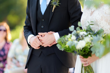 Bride and groom holding their hands during beautiful wedding ceremony on summer day outdoors.