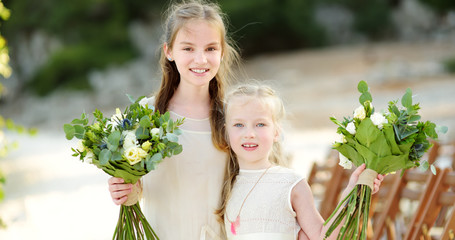 Two adorable young bridesmaids holding beautiful flower bouquets after wedding cemerony outdoors.