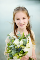 Adorable little bridesmaid holding beautiful flower bouquets after wedding cemerony outdoors.