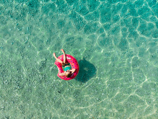 Aerial top down view of cute young girl floating on toy ring at Myrtos beach, the most beautiful beach of Kefalonia, a large coast with turqoise water and white coarse sand.