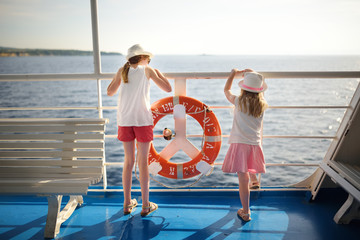 Adorable young girls enjoying ferry ride staring at the sea on sunset. Children having fun on...