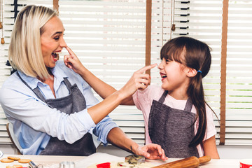 Mother and daugthter having fun cooking togather and learning to make a cake while baking in kitchen at home