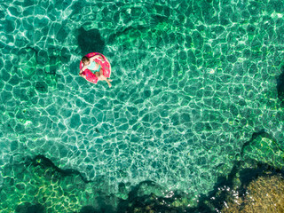 Aerial top down view of cute young girl floating on toy ring at Emplisi Beach, picturesque stony beach in a secluded bay, with clear waters popular for snorkelling.