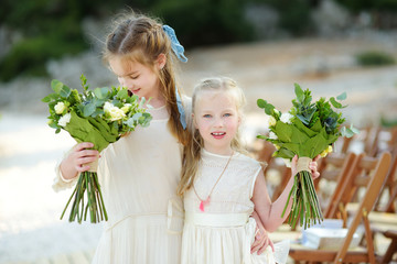 Two adorable young bridesmaids holding beautiful flower bouquets after wedding cemerony outdoors.