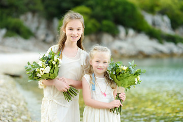 Two adorable young bridesmaids holding beautiful flower bouquets after wedding cemerony outdoors.
