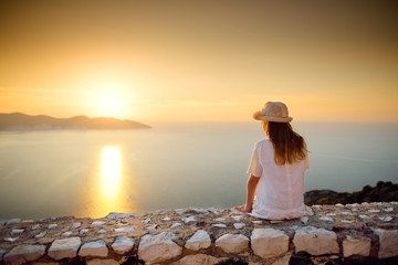 Cute young girl enjoying the view of picturesque jagged coastline of Kefalonia on summer sunset.
