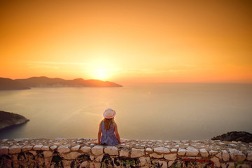 Cute little girl enjoying the view of picturesque jagged coastline of Kefalonia on summer sunset.