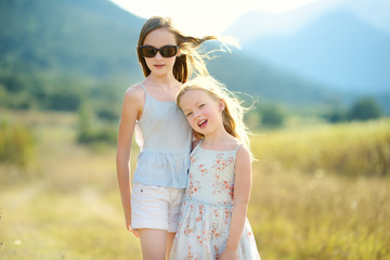 Two cute young sisters laughing and hugging on warm and sunny summer day during family vacations in Greece