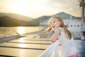 Adorable young girl enjoying ferry ride staring at the sea on sunset. Child having fun on summer family vacation in Greece.