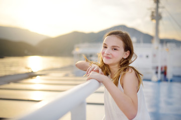 Adorable young girl enjoying ferry ride staring at the sea on sunset. Child having fun on summer family vacation in Greece.