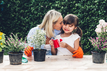Mother with little daughter having fun and planting flowers in pot with soil together,daughter...