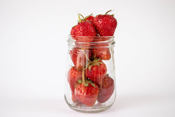 Strawberrys many with both ripe fruit and  not fruit ripe in jar glass and strawberrys all laid are on a white background.