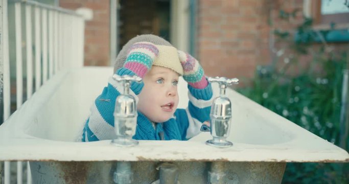 Little toddler in old bathtub outside removes his hat