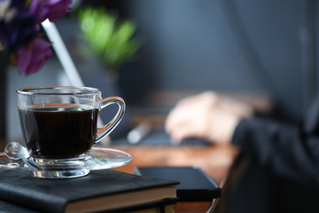 Coffee Mockup on the desk with staff is using a laptop in the office behind.
