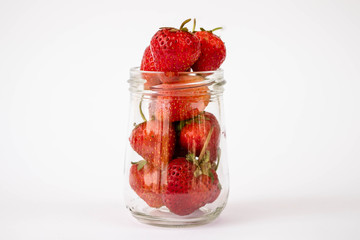 Strawberrys many with both ripe fruit and  not fruit ripe in jar glass and strawberrys all laid are on a white background.