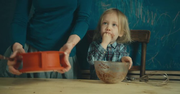 Mother putting dough in springform with toddler licking the bowl