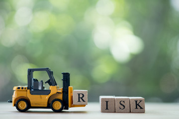 Toy forklift hold letter block R to complete word RISK.