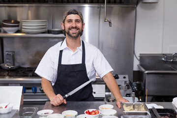 A happy smiling male chef in a restaurant kitchen holding a chefs knife.