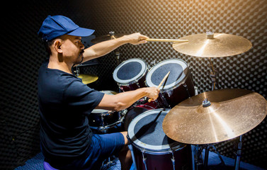 man put black t-shirt to playing the drum set with wooden drumsticks in music room