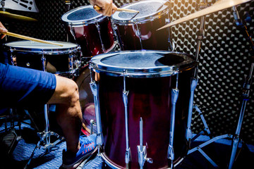 man playing the drum set with wooden drumsticks and bass drum with foot in music room