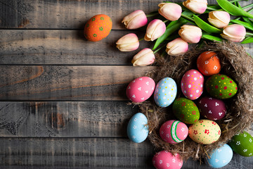 Happy easter! Colourful of Easter eggs in nest with Pink tulips and Feather on wooden background.